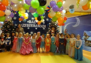 Grupa dzieci stoi z p. Agnieszką i p. Natalią na tle dekoracji, pomiędzy przystrojonymi choinkami.